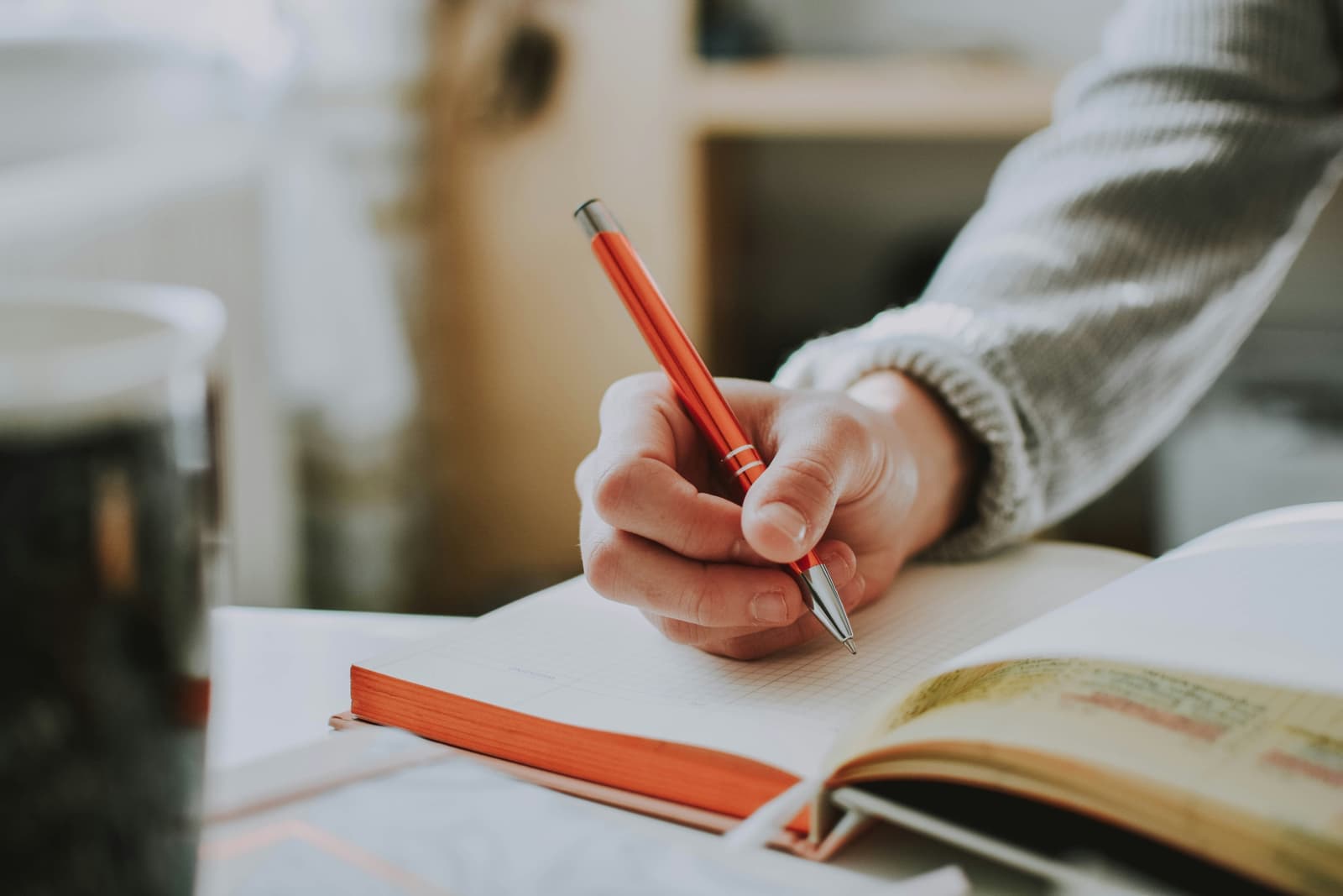 A close-up of a hand writing assessment notes with a red pen in a squared notebook